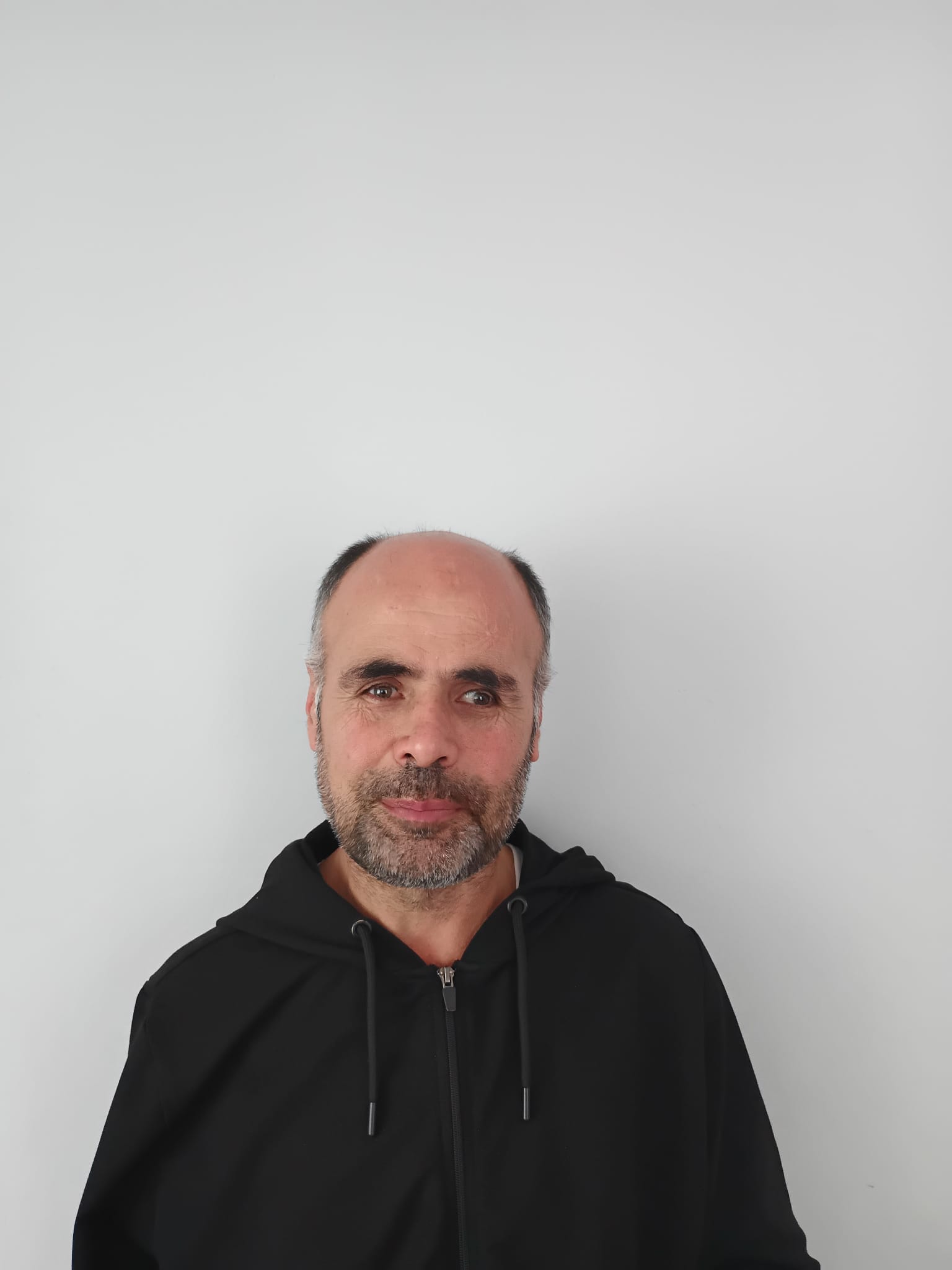 Siyah kapüşonlu bir giysi giymiş Habib Sincar'ın, sade beyaz bir arka plan önünde yakından çekilmiş görüntüsü.